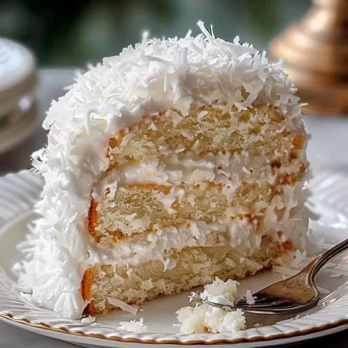 Delicious slice of Coconut Cloud Cake decorated with coconut flakes and cream.